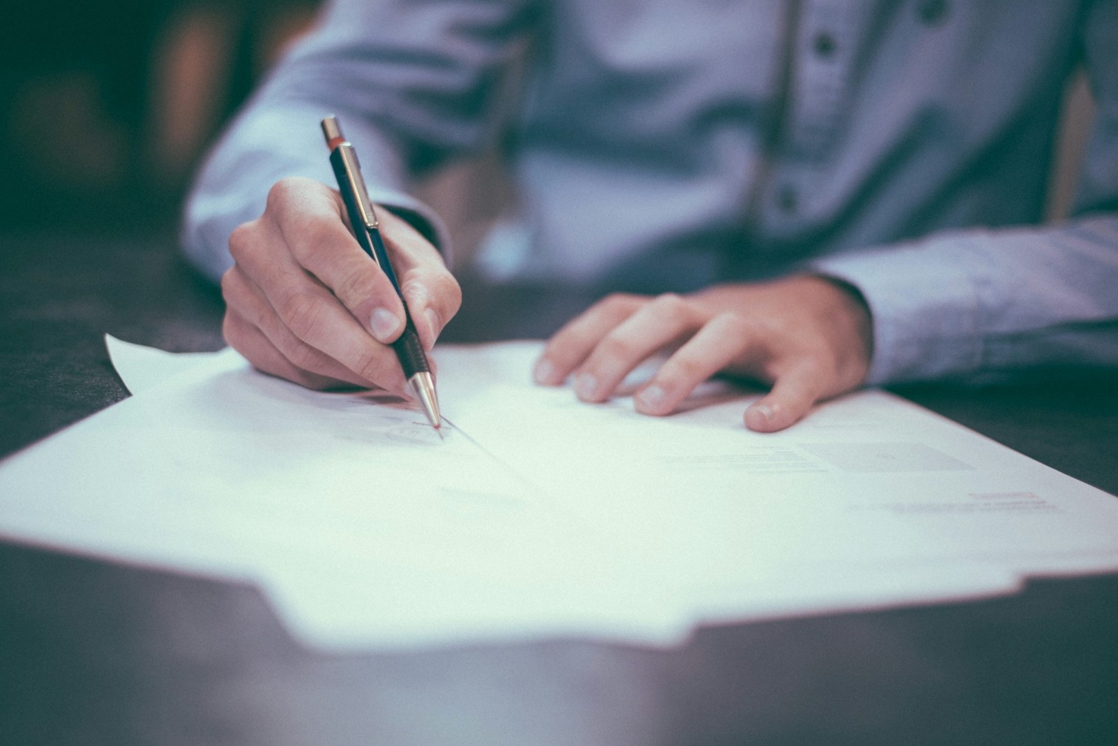 Close-up of hands writing on paperwork at a desk